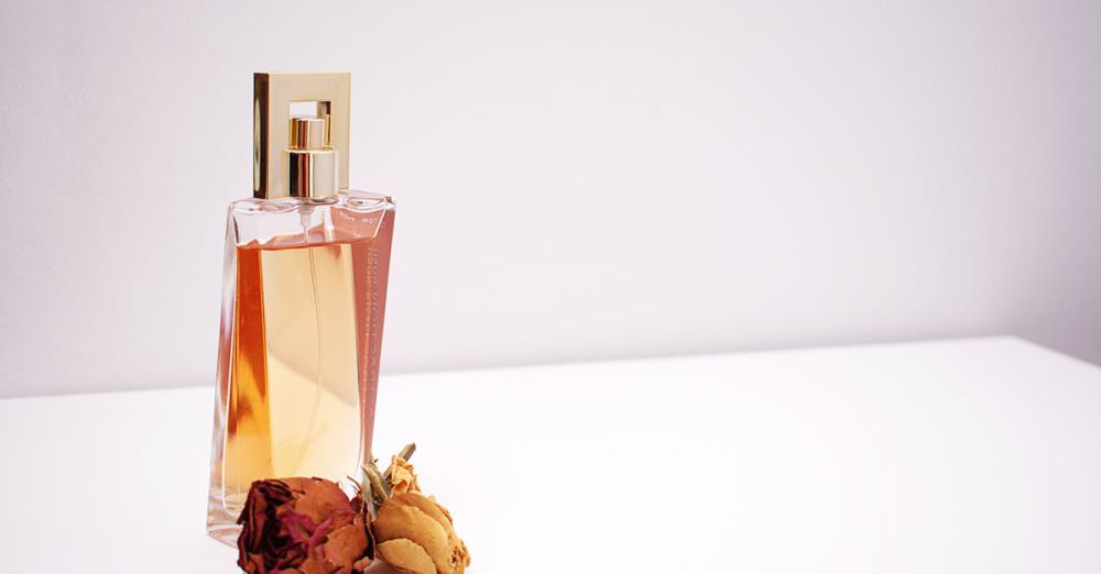 Perfumes - Elegant glass perfume bottle with luxurious design placed next to dried flowers against a minimalistic white background.