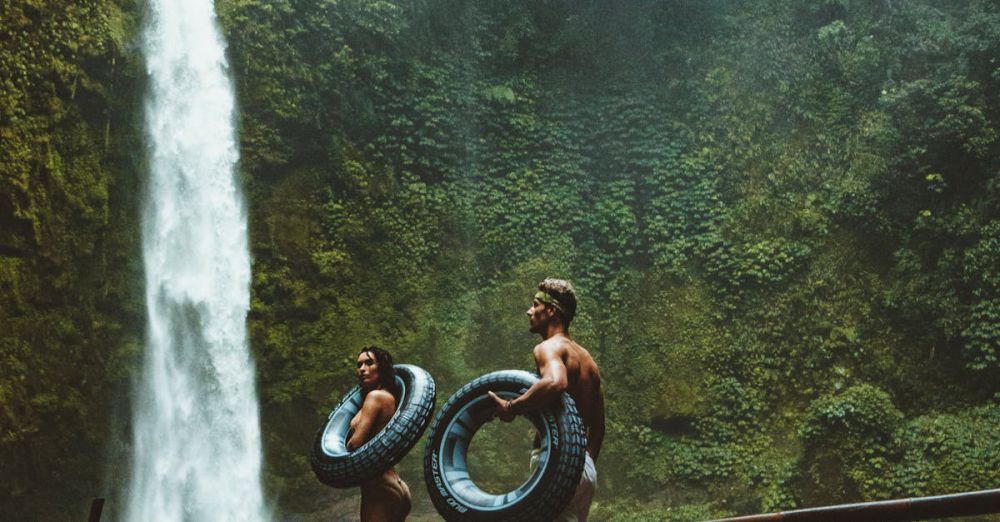 Adventure Waterfalls - A couple in swimwear with float tubes exploring a lush waterfall in Bali, Indonesia.