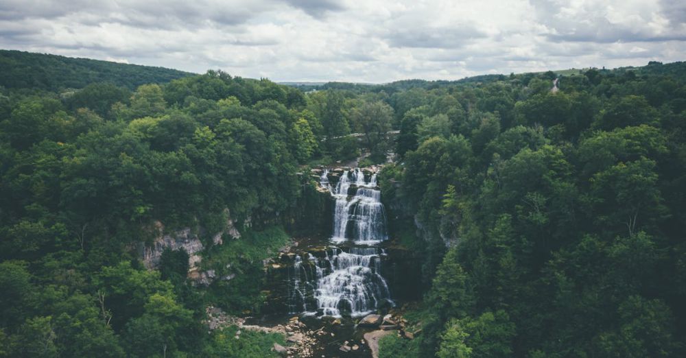 Popular Waterfalls - A breathtaking aerial shot of a waterfall surrounded by a dense, green forest.