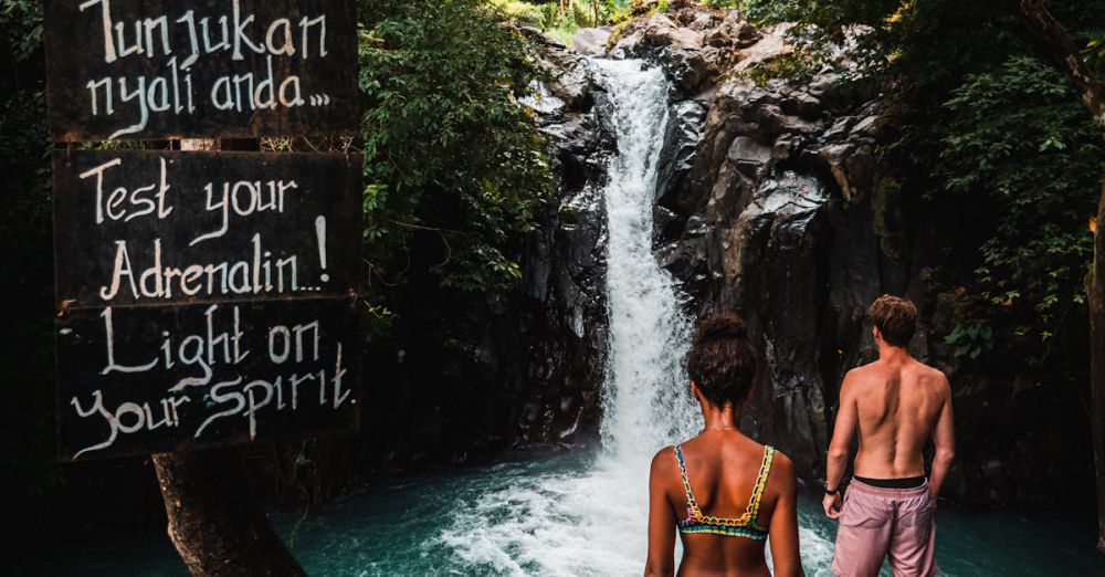 Romantic Waterfalls - A couple stands before a stunning waterfall in Bali, embracing adventure and nature.