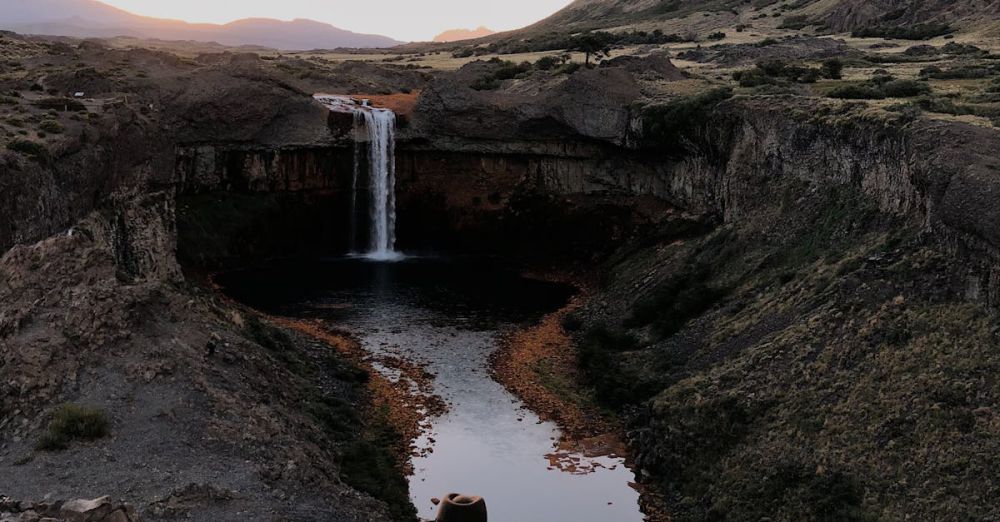 Spectacular Waterfalls - A lone traveler by a waterfall, surrounded by a dramatic landscape.