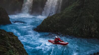 Kayaking Waterfalls - Dramatic scene of a man kayaking down waterfall surrounded by lush forest.