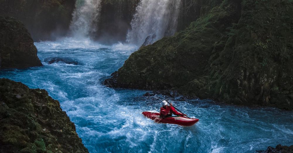 Kayaking Waterfalls - Dramatic scene of a man kayaking down waterfall surrounded by lush forest.