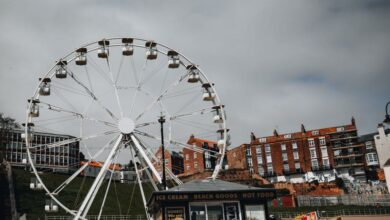 Family Tours - Ferris wheel at a beachside carnival with stalls and cloudy skies, capturing a fun festival vibe.