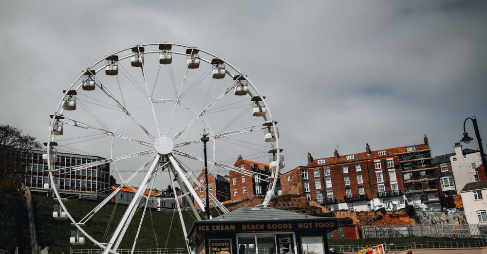 Family Tours - Ferris wheel at a beachside carnival with stalls and cloudy skies, capturing a fun festival vibe.