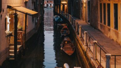 Scenic Tours - Tranquil view of a narrow canal in Venice at dusk, showcasing iconic gondolas and historic architecture.