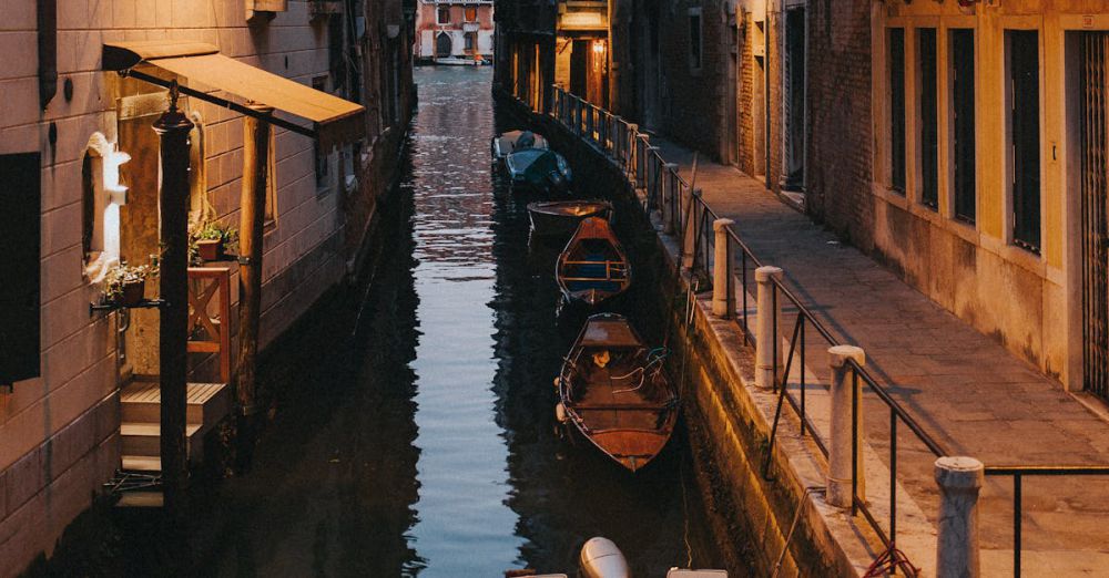 Scenic Tours - Tranquil view of a narrow canal in Venice at dusk, showcasing iconic gondolas and historic architecture.