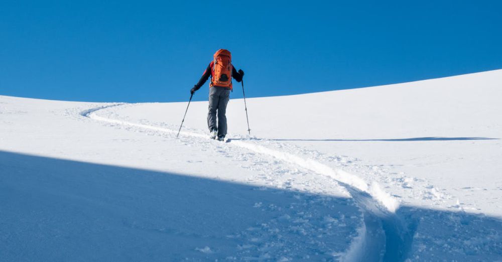 Solo Tours - A lone skier with a backpack traverses a snow-covered landscape under clear blue skies.