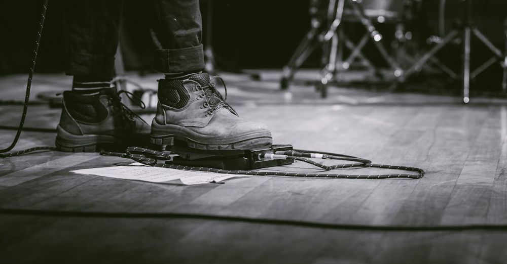 Live Music Tours - Black and white image of a performer using guitar pedal at a live concert.