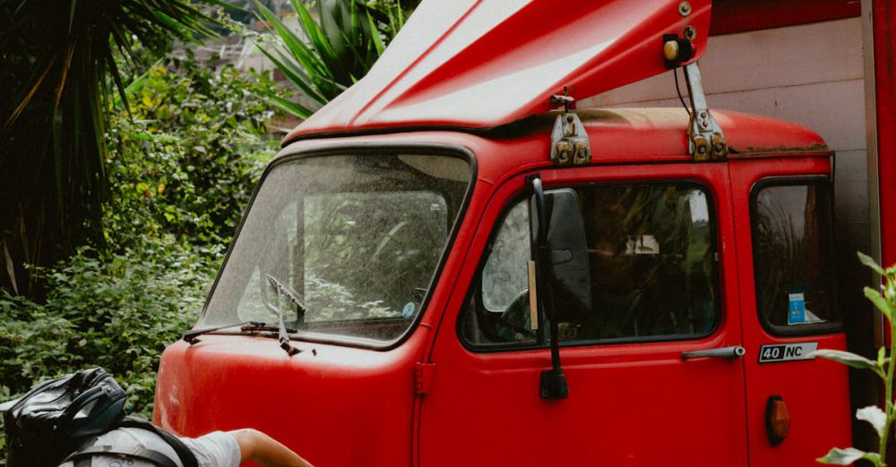 Finding Tours - Man inspecting a classic red truck amid lush greenery in Amalfi, Italy, on a sunny day.