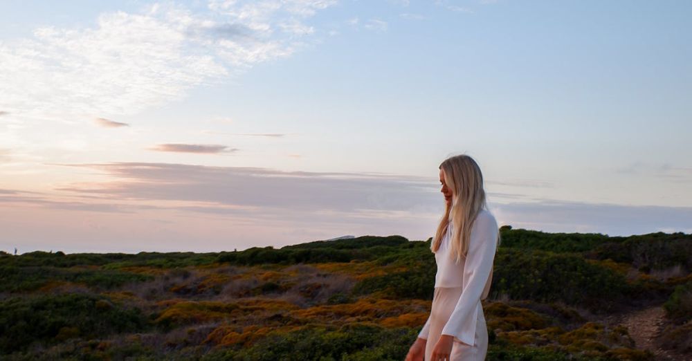 Weekend Escapes - A woman in white clothing walks on a dirt path during a beautiful sunset outdoors.