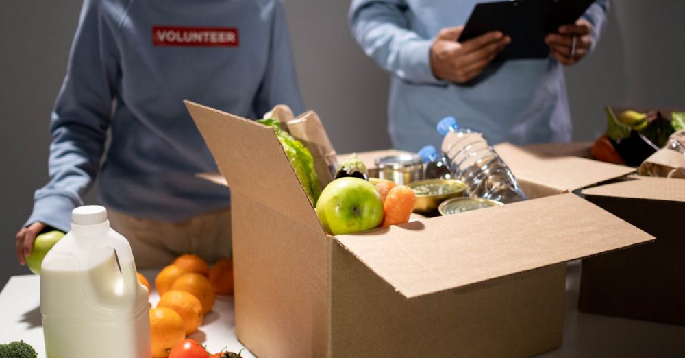 Canned Goods Markets - People packing a cardboard box with essentials like fruits, vegetables, and bottled water for charity.