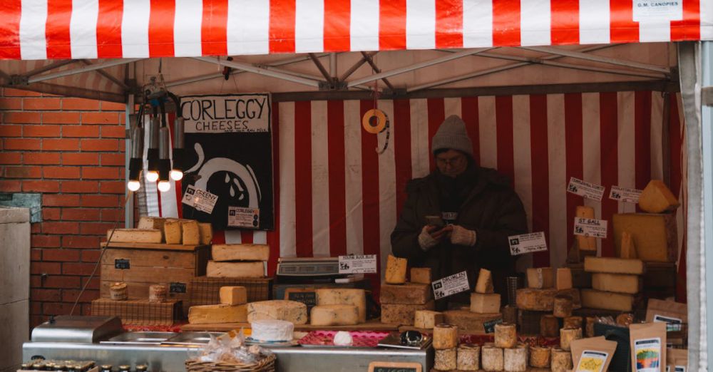 Cheese Markets - A bustling outdoor market stall selling various cheeses against a brick wall backdrop.