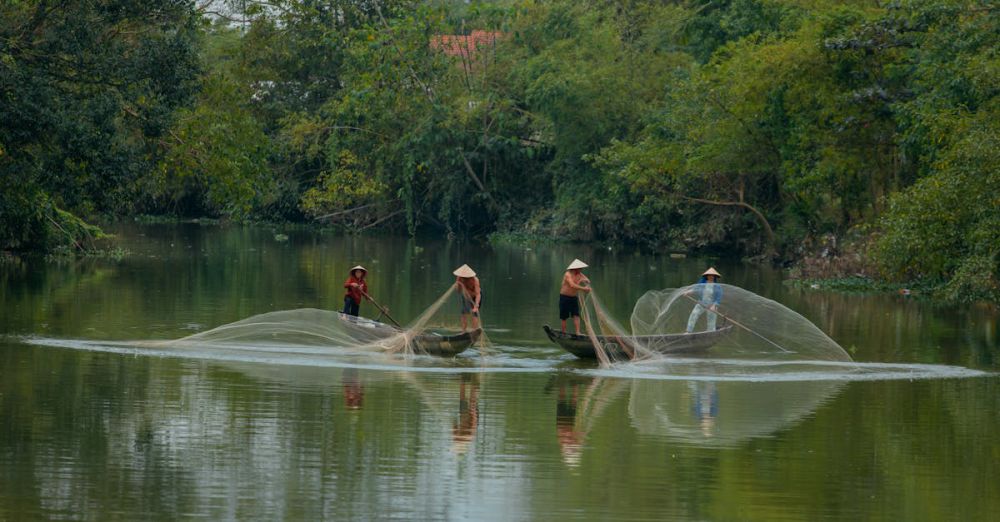 Scenic Canoe Portaging - Three Vietnamese fishermen in conical hats casting nets on the Perfume River, Huế, Vietnam.