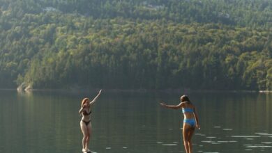 Ontario Canoe Portaging - Two women balance on a canoe in Killarney, Ontario, surrounded by serene lake and forest views.
