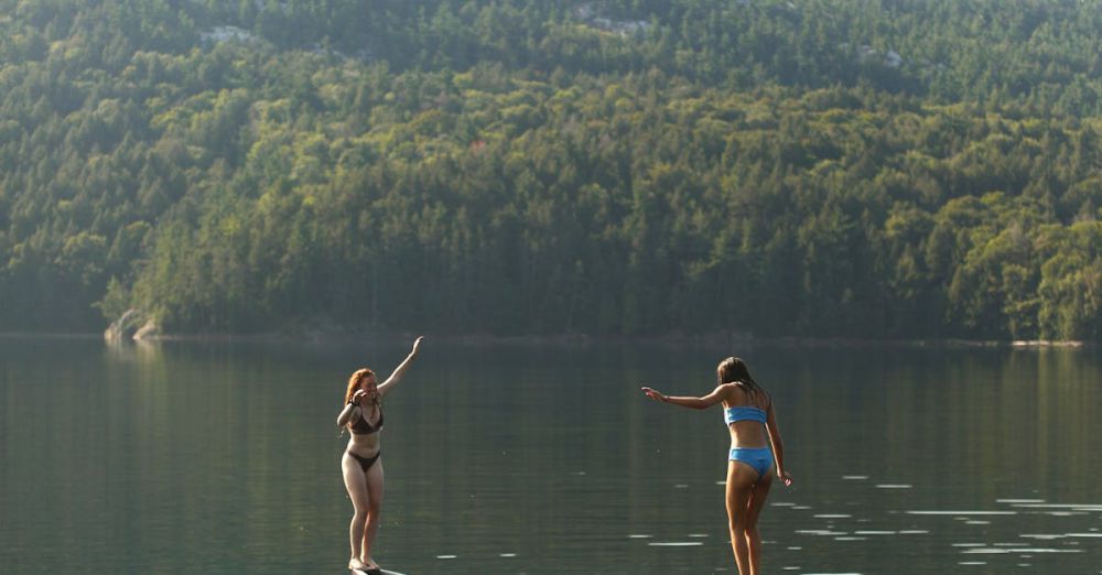 Ontario Canoe Portaging - Two women balance on a canoe in Killarney, Ontario, surrounded by serene lake and forest views.