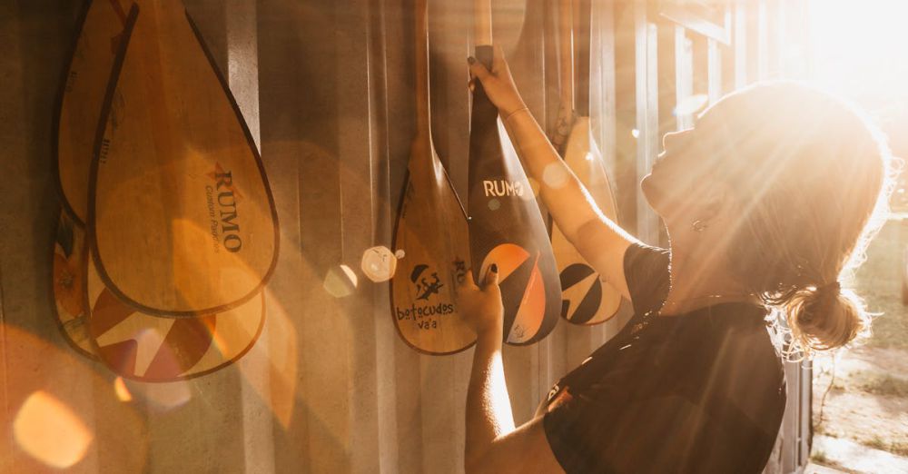 Canoe Selection - Side view of young female athlete taking wooden canoe oar from ribbed wall in back lit