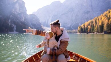 Family Canoe Portaging - A father and baby on a boat pointing at scenic mountain lake view in autumn.