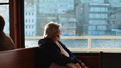 Portaging Safety - A senior woman wearing a mask gazes out the ferry window, reflecting by the sea.