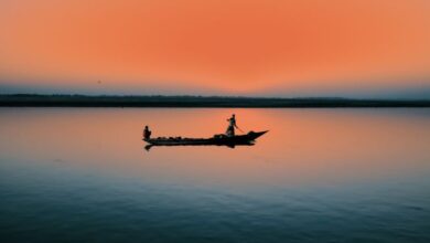 Fishing Canoe Portaging - Silhouette of a canoe at sunrise casting reflection on a placid lake.