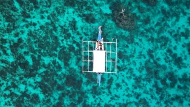 Island Portaging - Stunning aerial shot of a boat floating on vibrant blue waters above a coral reef, showcasing nature's beauty.