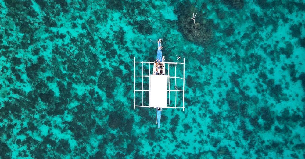 Island Portaging - Stunning aerial shot of a boat floating on vibrant blue waters above a coral reef, showcasing nature's beauty.