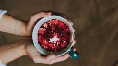 Popular Winter Festivals - A close-up of hands holding a mug filled with red glitter stars, ideal for festive and holiday themes.