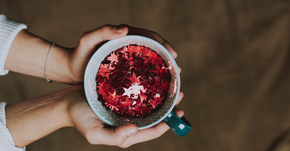 Popular Winter Festivals - A close-up of hands holding a mug filled with red glitter stars, ideal for festive and holiday themes.