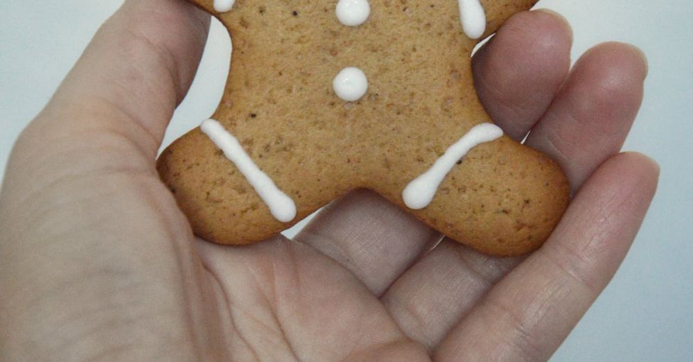 Food Winter Festivals - Close-up of a hand holding a gingerbread cookie with lights in the background.