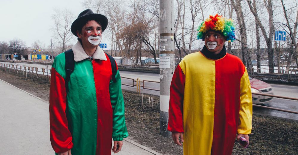 Comedy Winter Festivals - Two adults dressed as clowns walking outdoors in colorful costumes on a cloudy day.