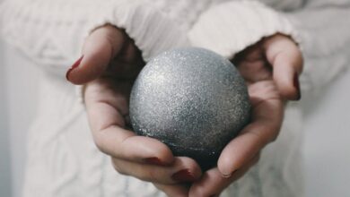 Artistic Winter Festivals - Close-up of female hands holding a glittery silver Christmas ornament in a cozy setting.