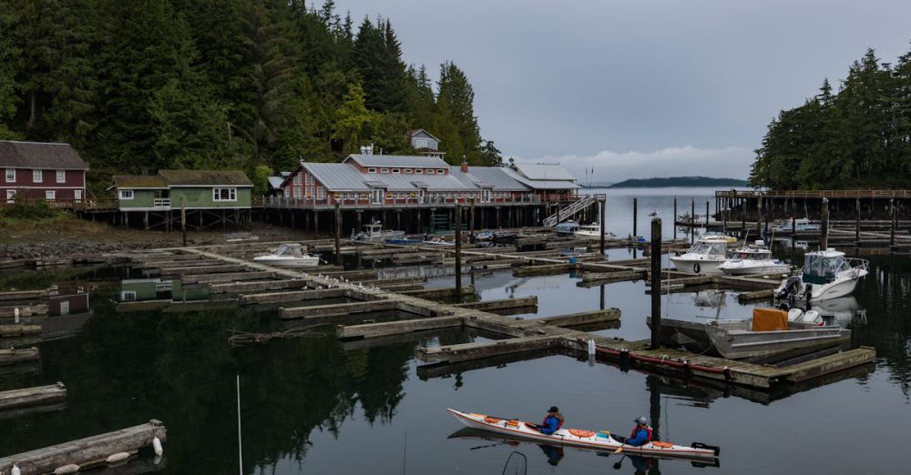 BC Scenic Train Rides - Serene view of Telegraph Cove's harbor in BC, Canada, featuring kayakers and rustic buildings.