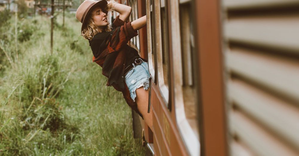 Scenic Views Scenic Train Rides - A joyful young woman embraces freedom as she leans out of a passenger train window traveling through lush countryside.