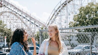 Weekend Scenic Train Rides - Two young women enjoying a sunny day at an amusement park, chatting happily near a rollercoaster.