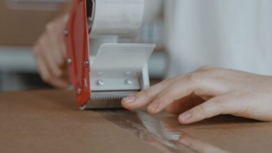 Tape Dispensers - A person sealing a cardboard box with a tape dispenser in an indoor setting.