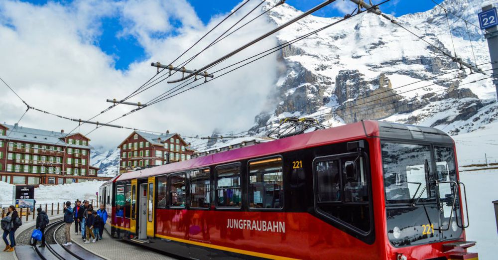 Glacier Scenic Train Rides - From below of contemporary train on railway near group of anonymous travelers on platform behind snowy mountain and buildings in winter