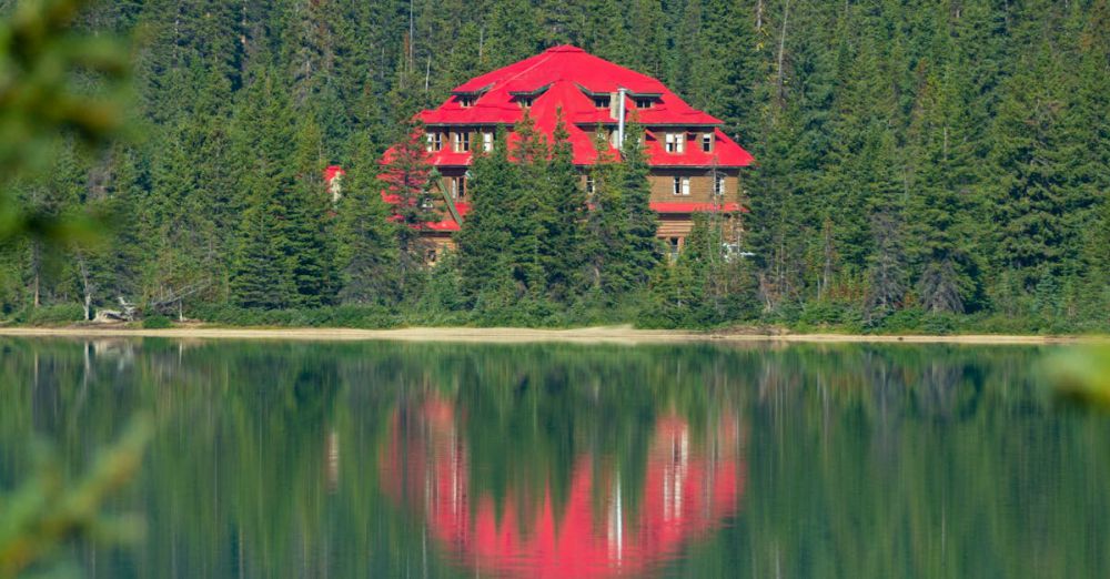 River Scenic Train Rides - Red lodge reflecting in calm lake amid lush forest in Jasper, Alberta.