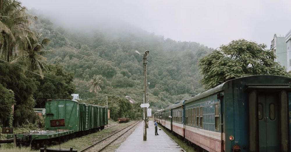 Remote Scenic Train Rides - A scenic train station surrounded by misty mountains in Qui Nhon, Vietnam, showcasing vintage locomotives and lush greenery.