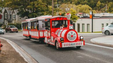 Quebec Scenic Train Rides - A vibrant red tourist train travels down a scenic street lined with trees on a sunny day.