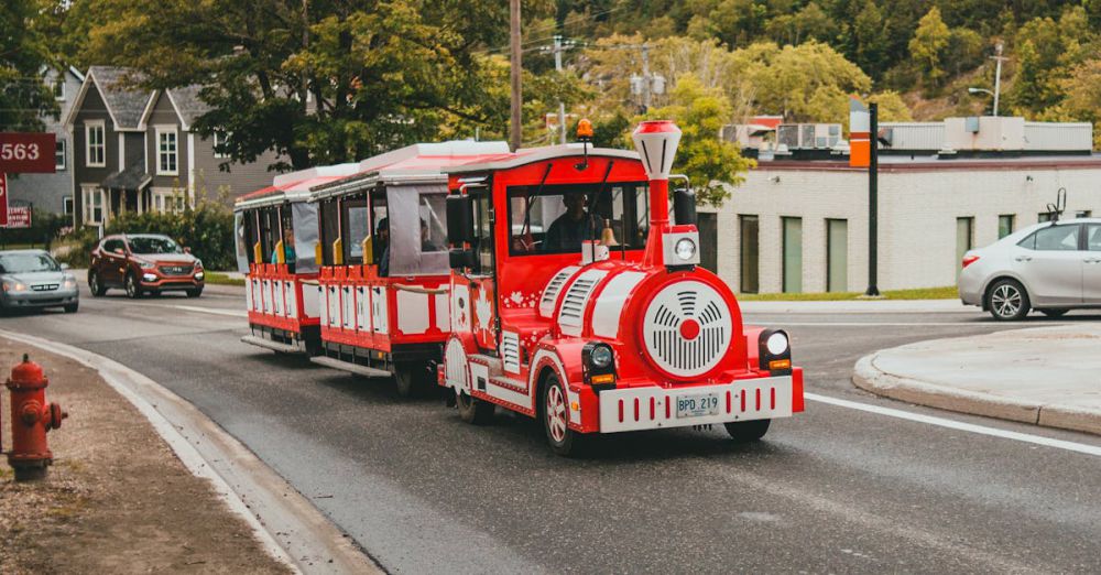 Quebec Scenic Train Rides - A vibrant red tourist train travels down a scenic street lined with trees on a sunny day.