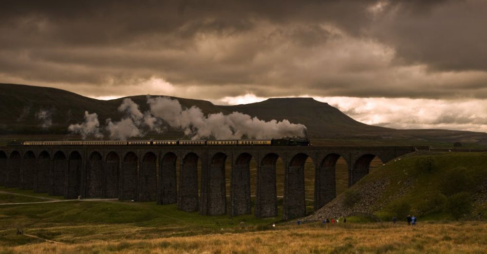 Historical Insights Scenic Train Rides - A steam train crosses a picturesque viaduct against a dramatic sky.