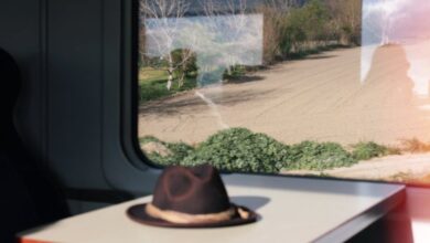 Solo Scenic Train Rides - Inside a train carriage, a lone hat rests on a table with fields visible through the window.