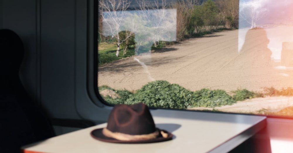 Solo Scenic Train Rides - Inside a train carriage, a lone hat rests on a table with fields visible through the window.