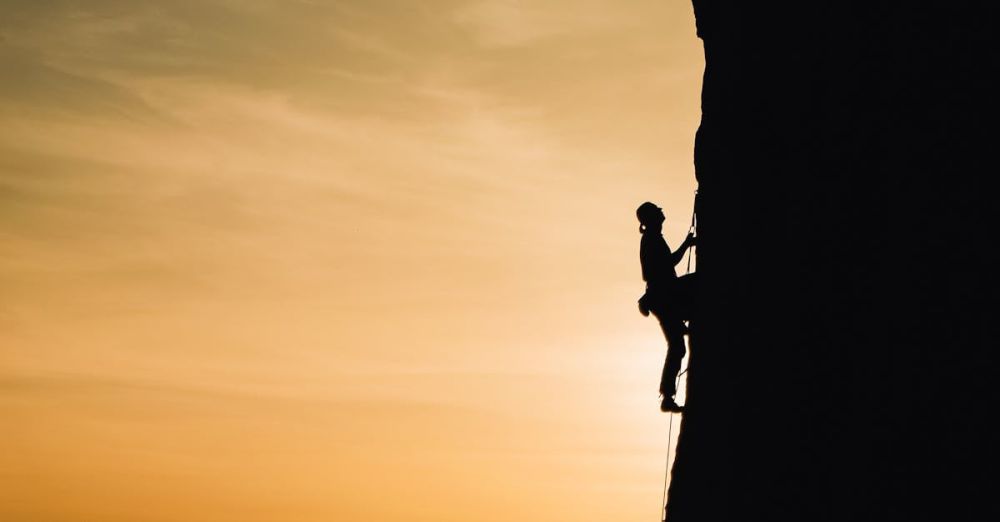 Rock Climbing - A silhouette of a rock climber scaling a steep cliff during sunset in Russia, showcasing determination and adventure.