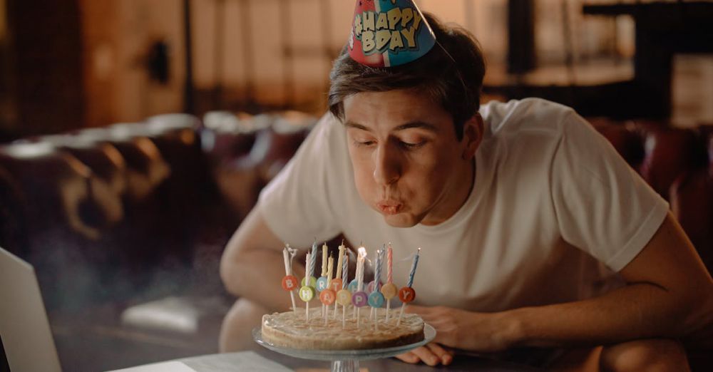 Tech Gifts - A young man celebrates his birthday with a cake and a laptop in a cozy home setting.