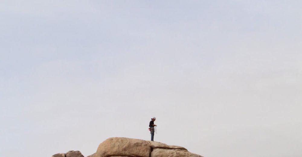 Multi-Pitch Rock Climbing - A lone person stands atop a rocky cliff, embodying adventure and solitude outdoors.