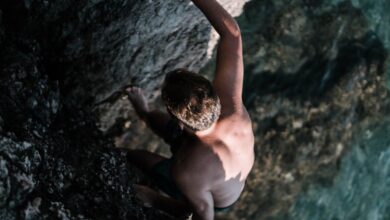 Bouldering Rock Climbing - A man confidently climbs a rocky cliff overlooking clear water.