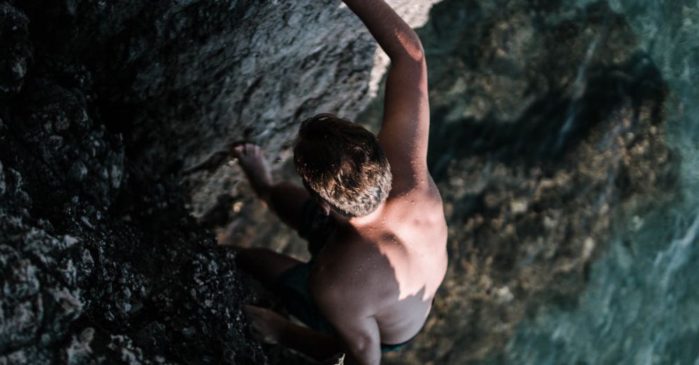 Bouldering Rock Climbing - A man confidently climbs a rocky cliff overlooking clear water.