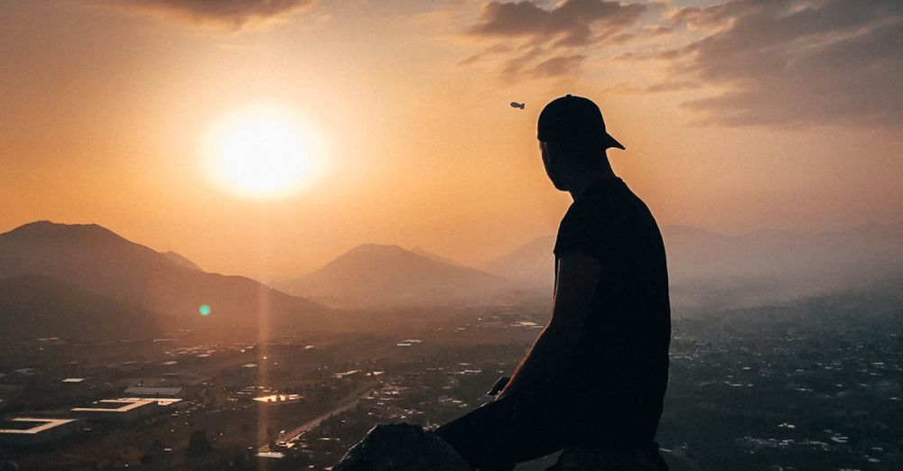 Sunset Rock Climbing - A man sits on a rock, silhouetted against a stunning sunset over a mountain landscape.