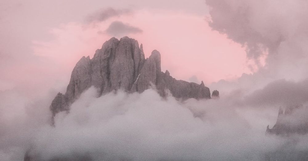 Scenic Rock Climbing - Breathtaking twilight view of a misty mountain peak surrounded by clouds.